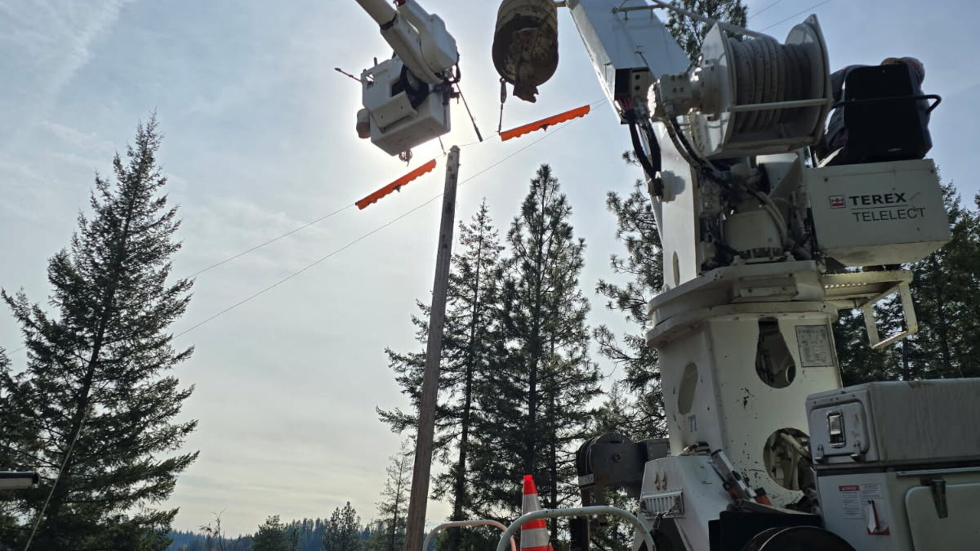 Digger derrick and bucket boom installing a wood utility pole on a wooded hillside