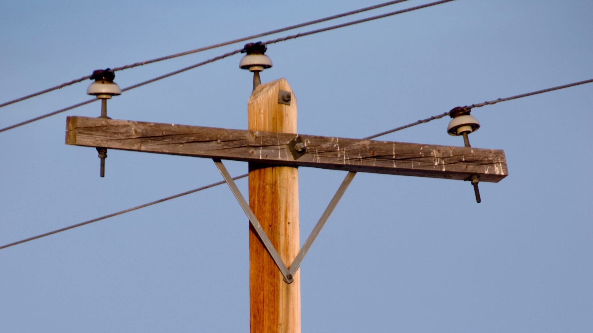 Weathered wooden utility pole with crossarm and porcelain insulators against a clear blue sky