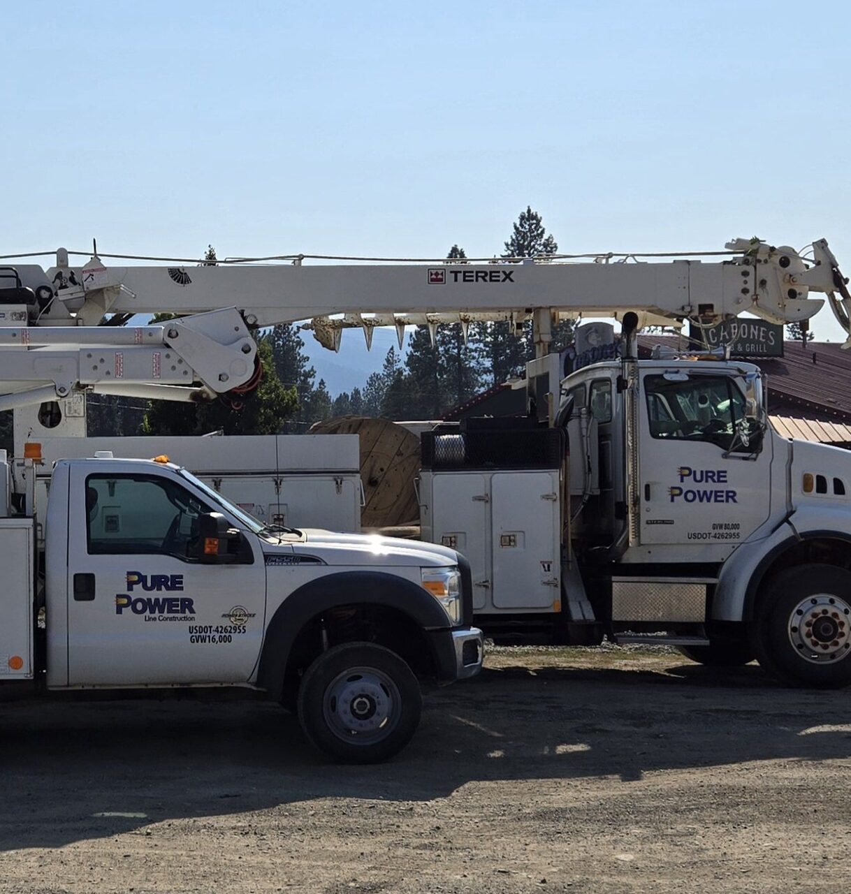 Branded Pure Power Line Construction service trucks, including a digger derrick, parked outdoors in North Idaho