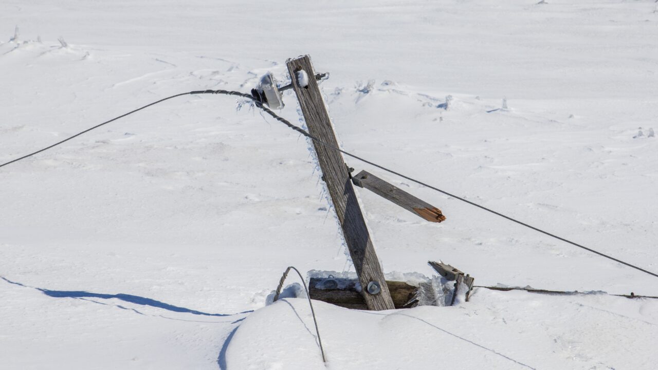 Iced, storm-damaged wooden utility pole and sagging lines in deep snow
