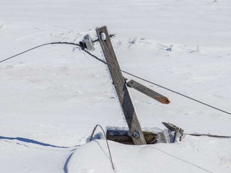 Iced, storm-damaged wooden utility pole and sagging lines in deep snow